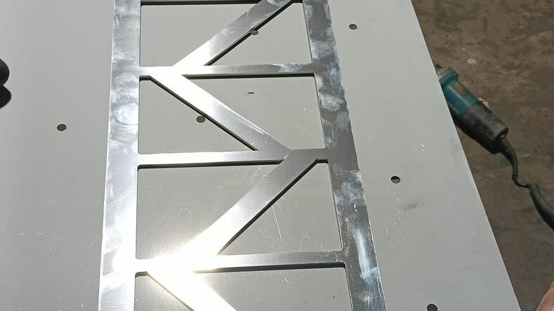 A profiled aluminium panel from project D022 laid on its setting-out template for checking in the workshop.