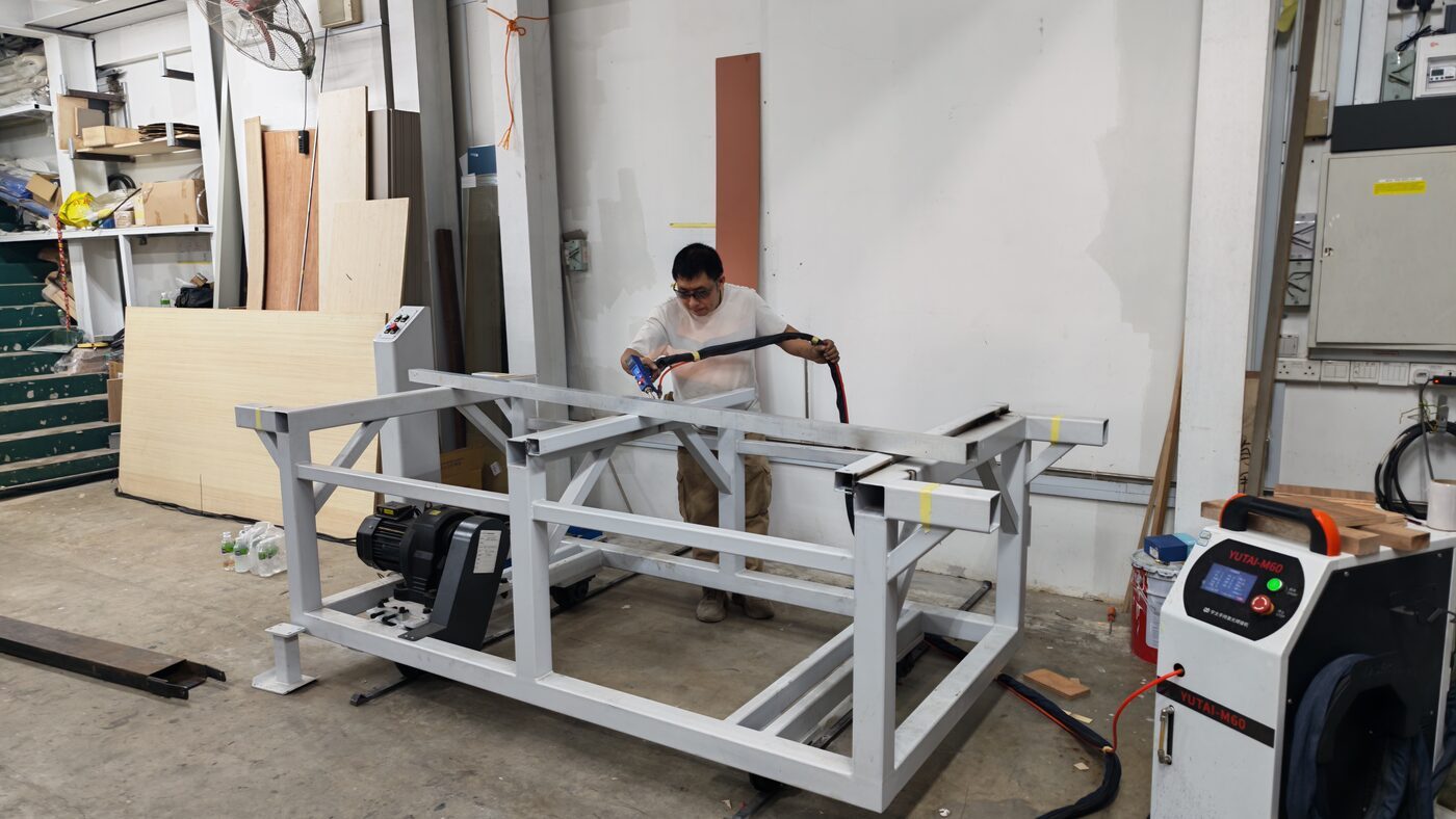 Laser Welding Stainless Steel and Aluminium: Low-Distortion Seams for Finish-Critical Work A fabricator using a handheld fibre laser welder on a steel frame assembly in the Rongda Pacific workshop.