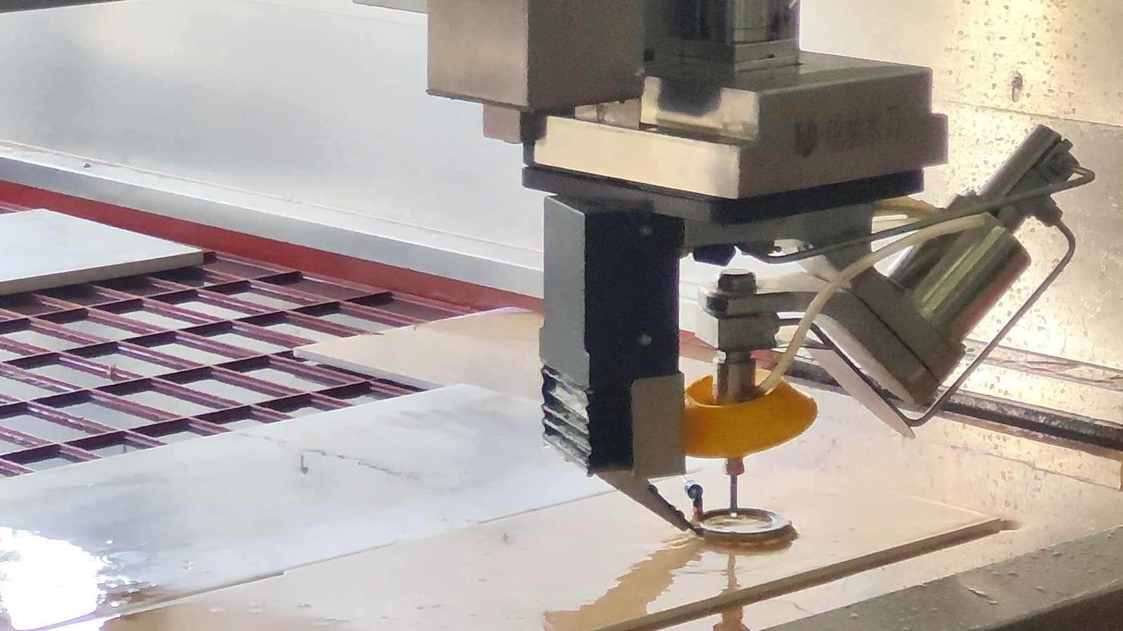 A waterjet cutting head at work on a wet cutting table, cutting without applying heat to the material.
