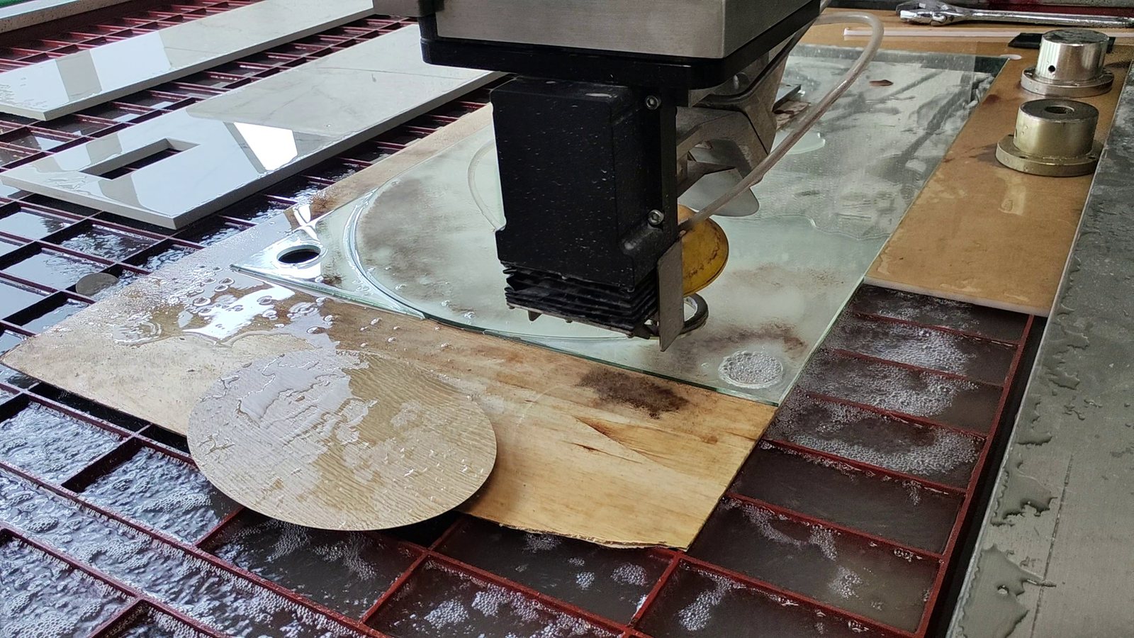 An abrasive waterjet cutting head working on a wet slatted cutting table, with finished cut pieces alongside.
