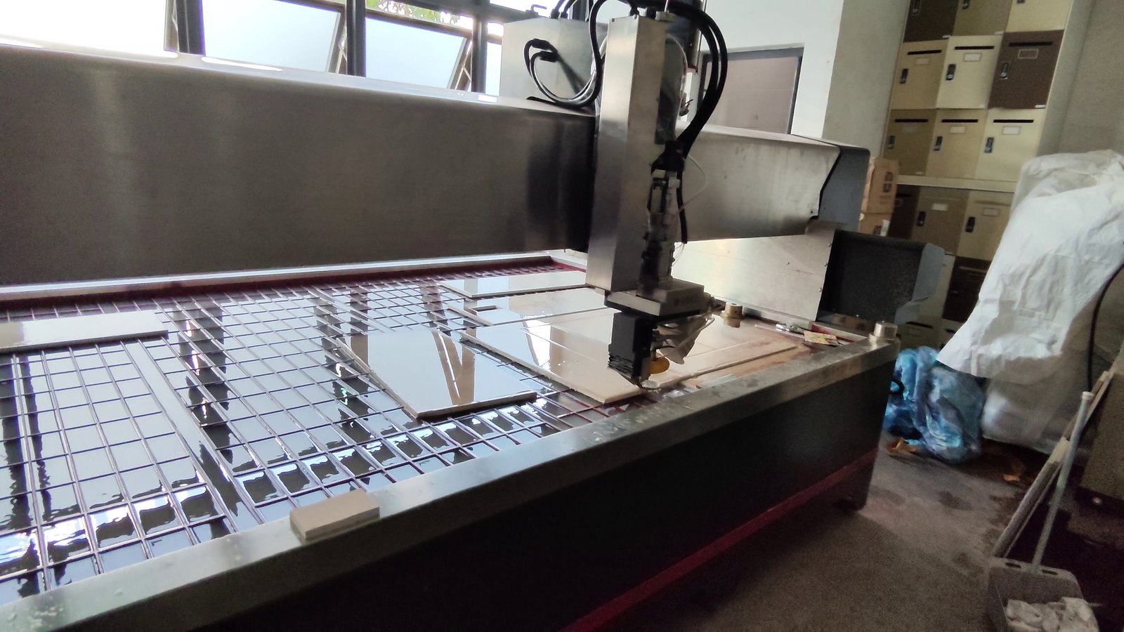 A waterjet cutting head profiling a large slab on a wet slatted table, with finished cut pieces alongside.