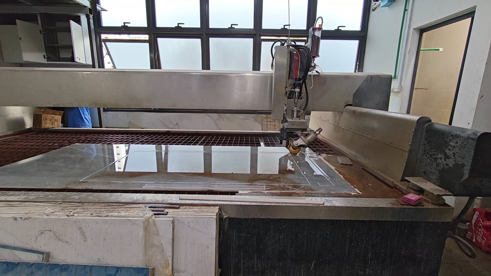 A large slab being profiled on the waterjet table, showing the wet slatted bed and the gantry-mounted cutting head.