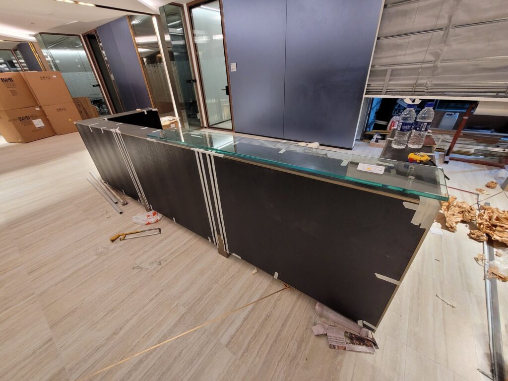 Builder’s Works for Furniture Installation: The Hidden Work That Determines Project Success Reception counter being installed with its glass top and protective packaging still in place